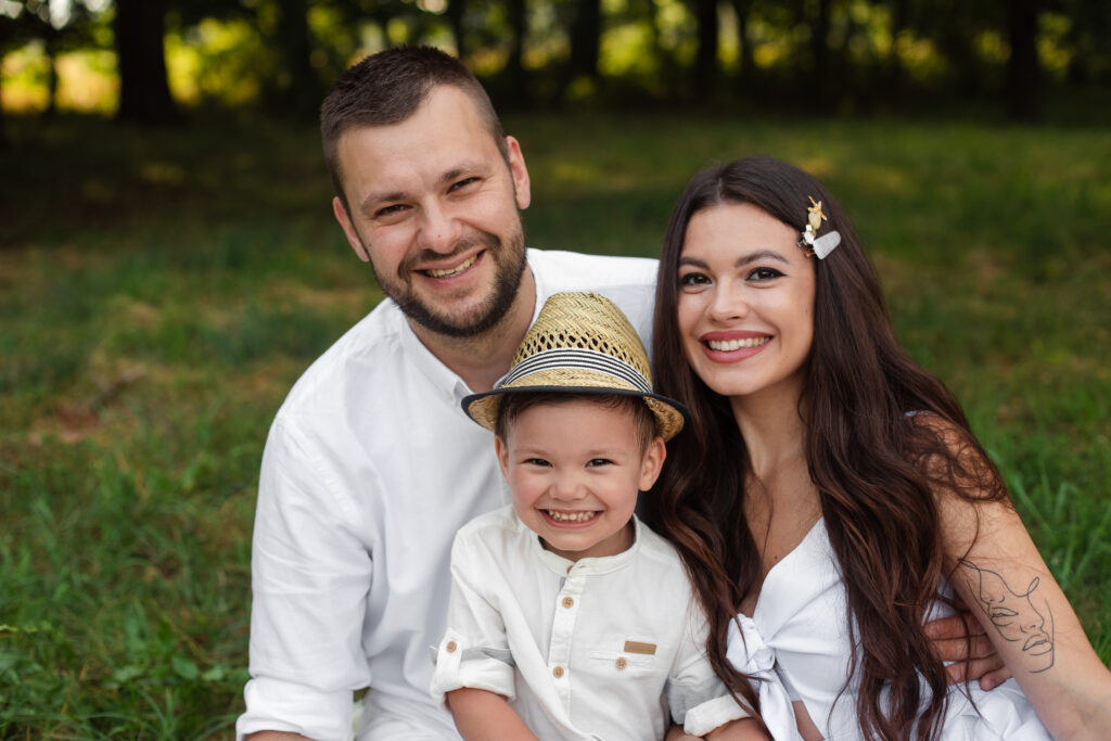 Stock photo headshot of a lovely Caucasian family of mother, father and their son smiling happily at camera in the park on summer day.